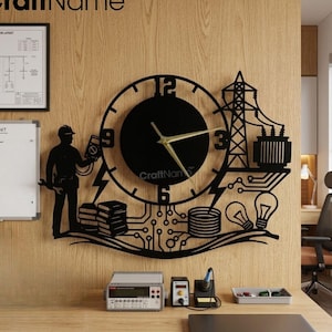 Op de afbeelding: Zwarte metalen wandklok met een thema van elektrotechniek. De klok heeft een ronde wijzerplaat met gouden wijzers, omgeven door silhouetten van een elektricien, elektriciteitsleidingen en gloeilampen. De tekst "CraftName" is zichtbaar.