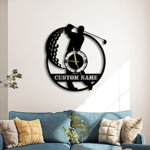 May include: Black and white silhouette of a golfer swinging a club with a golf ball in the background. The silhouette is part of a clock face with the words "CUSTOM NAME" printed below the clock face.