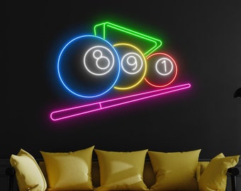 May include: Neon sign depicting a pool cue and three billiard balls with the numbers 8, 9, and 1. The balls are in different colors, and the cue is pink. The sign is mounted on a black wall above a yellow couch.