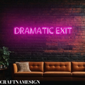 May include: A neon sign in bright pink letters reads "DRAMATIC EXIT" against a brick wall. Below the sign is a brown sofa with a fluffy pillow. The sign is a decorative element for a home or business.