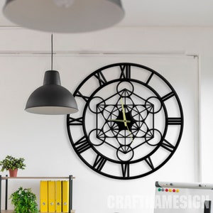 May include: Black metal wall clock with Roman numerals and a geometric design in the centre. The clock is hanging on a white wall.