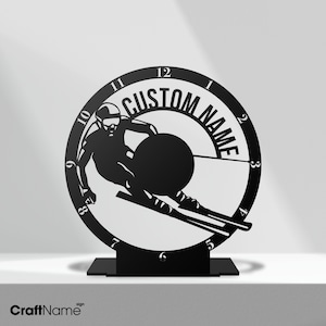 May include: Black metal clock with a skier silhouette and the text "CUSTOM NAME" on the face. The clock is on a black stand.