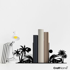 May include: Black metal bookends shaped like alligators with palm trees and a sun. The bookends are holding up four books.