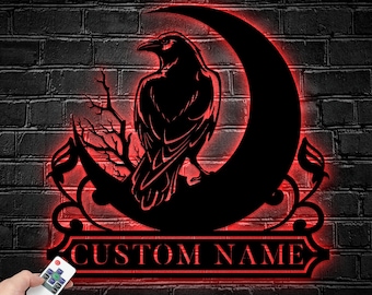 May include: A black wall sign featuring a silhouette of a raven perched on a crescent moon with bare branches and decorative flourishes. The sign emits a red glow and includes a rectangular banner with the text CUSTOM NAME and a remote control.