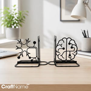 May include: A pair of black metal bookends featuring intricate cut-out designs. One bookend displays a stylised neuron structure, while the other depicts a human brain with circuit-like patterns. Both pieces have a flat base for stability.