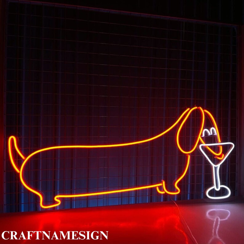 May include: A neon sign featuring a dachshund dog holding a martini glass. The dog and glass are outlined in bright orange and white neon against a dark background. The sign includes the text "CRAFTNAMESIGN" at the bottom.