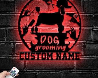 Puede incluir: Un letrero de pared circular de metal negro con la silueta de un caniche sobre una plataforma, rodeado de herramientas de aseo como tijeras, un cepillo y un secador. El texto dice DOG grooming CUSTOM NAME, iluminado con luz LED roja.