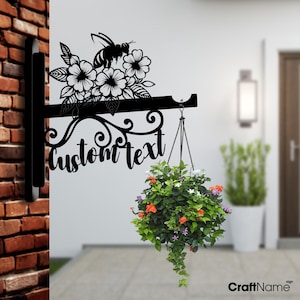 May include: Black metal sign with a bee and flowers design. The sign has a hanging planter and says "custom text".