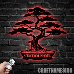 May include: A black metal silhouette of a bonsai tree with a red glow. The tree is in a pot with the text "CUSTOM NAME" on it. The image is on a brick wall background.