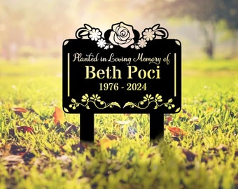 May include: Black metal garden stake with a white rose and floral design. The stake has the text "Planted in Loving Memory of Beth Poci 1976 - 2024".