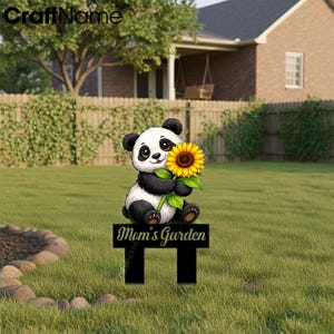 Op de afbeelding: Een tuinbord met een cartoon panda die een gele zonnebloem vasthoudt. De panda heeft zwart-witte vacht en staat boven een zwart rechthoekig bord met de witte tekst Mom's Garden in een cursief lettertype.
