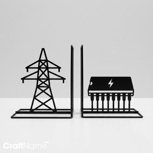 May include: A pair of black metal bookends. One bookend features a silhouette of an electrical transmission tower. The other bookend displays a silhouette of an integrated circuit chip with a lightning bolt symbol centered on its top surface.