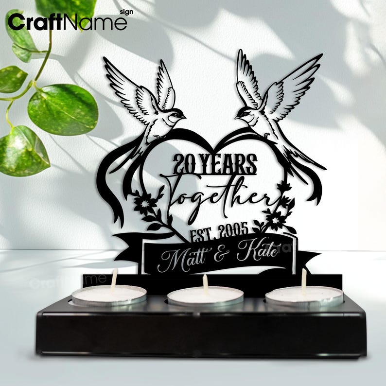 Puede incluir: Portavelas de madera negra con tres velas encendidas. Encima de las velas hay un recorte de metal negro con dos p&aacute;jaros, un coraz&oacute;n y las palabras "20 YEARS Together EST. 2005 Matt & Kate."