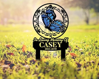 Può includere: Un picchetto commemorativo da giardino in metallo nero con una cornice circolare, un bordo in filigrana e una farfalla blu. Sotto il cerchio, una targa rettangolare riporta il testo In Loving Memory Of CASEY 2012-2019.