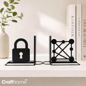 May include: A pair of black metal bookends featuring a padlock silhouette on one side and a geometric atom-like structure with interconnected circles and lines on the other. Both pieces have a flat base and a vertical support panel.