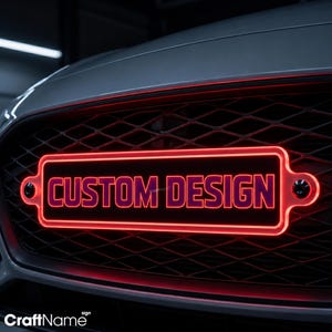 May include: A rectangular vehicle grille emblem featuring a bright red neon-style border and the text CUSTOM DESIGN in bold red lettering. The emblem is mounted onto a black diamond-patterned mesh grille with two visible black mounting screws.