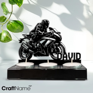 Könnte beinhalten: Schwarze Silhouette einer Person, die ein Motorrad fährt, mit dem Namen "DAVID" darunter. Das Motorrad steht auf einem schwarzen Holzsockel mit drei Kerzenhaltern.
