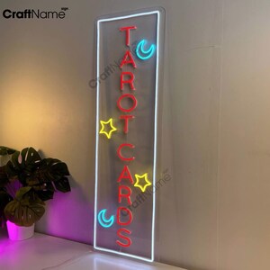 May include: Neon sign with the words "TAROT CARDS" in red letters, with a yellow star and blue crescent moon on either side of the letters.