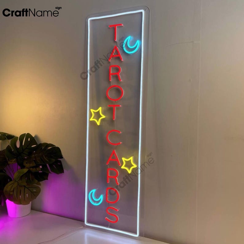 May include: Neon sign with the words "TAROT CARDS" in red letters, with a yellow star and blue crescent moon on either side of the letters.