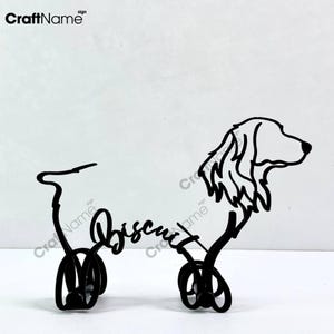 May include: Black metal silhouette of a dog with the name "Biscuit" written in cursive. The dog is standing on four legs with wheels.