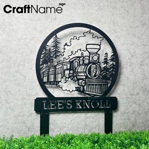 May include: Black metal sign featuring a train scene within a circular frame, with trees and smoke details. The sign includes the text "LEE'S KNOLL" on a rectangular base, suitable for outdoor display.