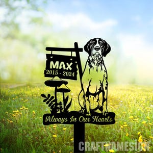 May include: Black metal silhouette of a dog with the name Max and dates 2015-2024 on a sign. The sign is attached to a metal stake with a mushroom and leaves. The sign also reads "Always In Our Hearts".