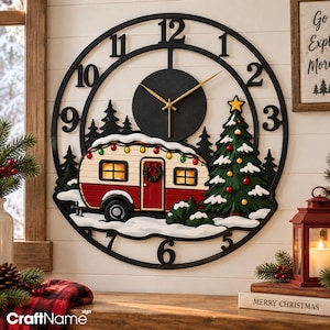 May include: A round wall clock with a black frame and numerals featuring a central black dial with gold hands. The design depicts a red and white vintage camper trailer, a decorated Christmas tree, and pine trees set in a snowy landscape.