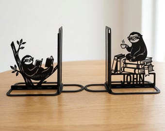 May include: A pair of black metal bookends featuring laser-cut sloth designs. One bookend shows a sloth in a tree reading a book, while the other depicts a sloth wearing glasses, sitting on a stack of books with a coffee cup and the name JOHN.
