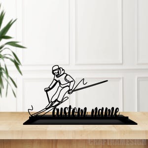 May include: Black metal silhouette of a skier in mid-air, with a ski pole and skis, on a black base with the text "custom name".
