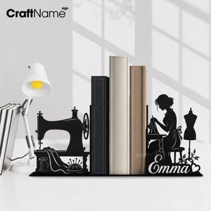 May include: A black metal bookend set featuring a vintage sewing machine on one side and a silhouette of a person sewing at a table with a dress form on the other. The name Emma is written in script font with a heart icon at the end.