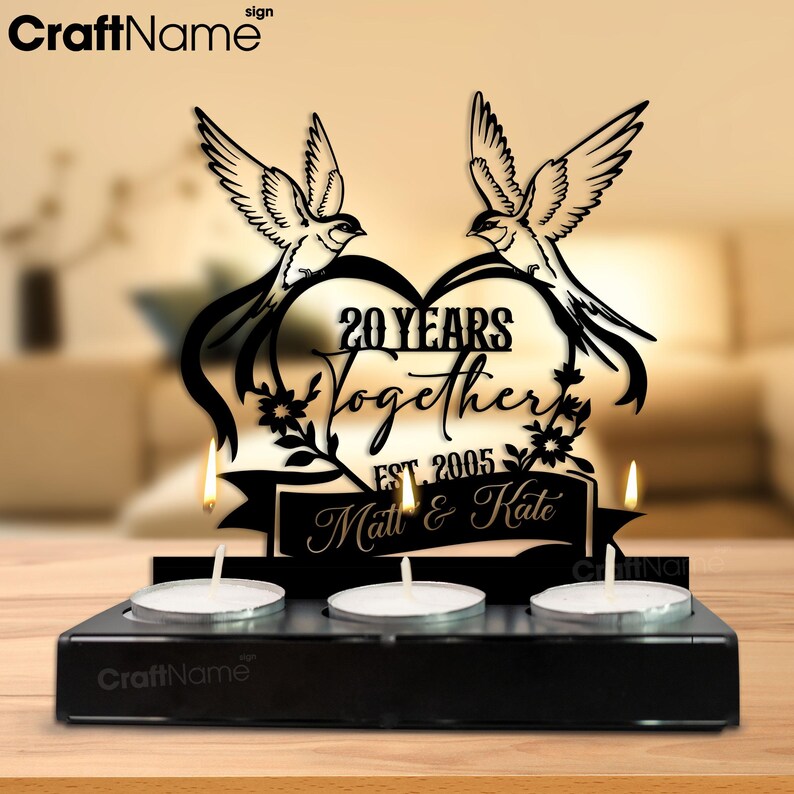 Puede incluir: Portavelas de metal negro con tres velas de t&eacute;. La pieza central presenta un dise&ntilde;o en forma de coraz&oacute;n con dos p&aacute;jaros, el texto "20 YEARS Together EST. 2005 Matt & Kate". Un art&iacute;culo decorativo para un aniversario de bodas.