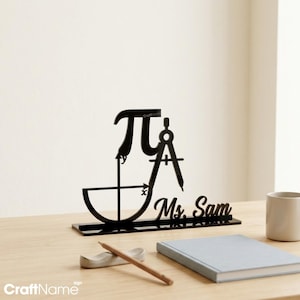 May include: A black acrylic desk sign featuring the mathematical pi symbol, a coordinate plane with x and y axes, a drafting compass, and the name Ms. Sam in cursive script, all mounted on a rectangular base for display on a flat surface.