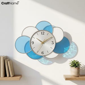 May include: A wall clock shaped like a cloud with overlapping circular frames in white and shades of blue. The central circular clock face is silver with gold hands and black numerals at 3, 6, 9, and 12. The CraftName sign logo is visible.