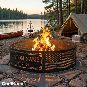 May include: A circular metal fire pit ring featuring a laser-cut American flag design and the text CUSTOM NAME EST. 2026. The black steel structure surrounds a bright, active campfire with visible flames and burning logs in the center.