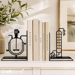 Puede incluir: Un par de sujetalibros de metal negro con diseños de ingeniería química industrial. El sujetalibros izquierdo muestra un recipiente de mezcla con agitador, el derecho una columna de destilación. Sostienen cuatro libros de color beige.