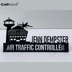 May include: A black metal desk sign featuring a silhouette of an airport control tower and an airplane. The text reads JENN DEMPSTER and AIR TRAFFIC CONTROLLER in a bold, sans-serif font. The design is mounted on a rectangular base.