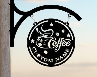 May include: A black circular metal sign hanging from a matching curved wall bracket. The sign features a graphic of a steaming coffee cup, coffee beans, stars, and the text Coffee and CUSTOM NAME in a bold, white, cut-out style font.