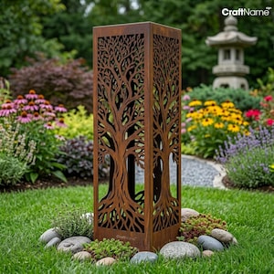 May include: A tall, rectangular, rust-coloured metal garden sculpture featuring an intricate, laser-cut design of a tree with sprawling branches and roots. The structure has an open-frame construction and is positioned upright on a green lawn.