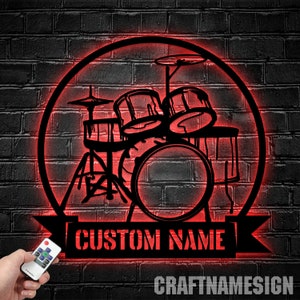以下が含まれることがあります： 「CUSTOM NAME」と書かれたバナーと、その下に「CRAFTNAMESIGN」というテキストが書かれた、赤い照明付きの金属製のドラムセットのシルエットです。