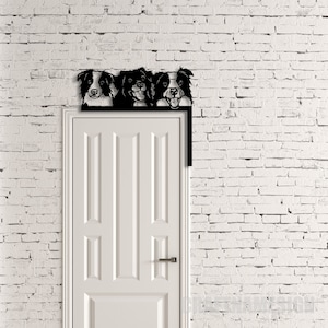 K&ouml;nnte beinhalten: Ein schwarzer Metall-T&uuml;rtopper mit drei Border-Collie-Hunde-K&ouml;pfen, die &uuml;ber die Oberseite schauen. Der T&uuml;rtopper ist &uuml;ber einer wei&szlig;en T&uuml;r mit einer wei&szlig;en Backsteinwand dahinter montiert.
