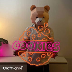 May include: A neon sign shaped like a cookie with the word "COOKIES" in pink neon lettering. The cookie is outlined in orange neon.