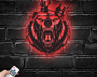 May include: A wall-mounted LED sign featuring a black graphic illustration of a roaring bear wearing a crown, illuminated by a vibrant red light. The sign is accompanied by a small handheld remote control with multiple buttons for light settings.