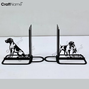 Op de afbeelding: Een paar boekensteunen van zwart metaal met silhouetten van jachthonden. De linker boekensteun toont een zittende hond, terwijl de rechter een hond met wild in de bek afbeeldt, met de naam NITRO in hoofdletters op de basis gedrukt.