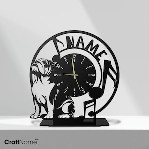 Puede incluir: Reloj de metal negro con una silueta de bulldog y notas musicales. La esfera del reloj tiene agujas y números dorados. El reloj está sobre un soporte negro y tiene una placa de nombre personalizada que dice "NAME".