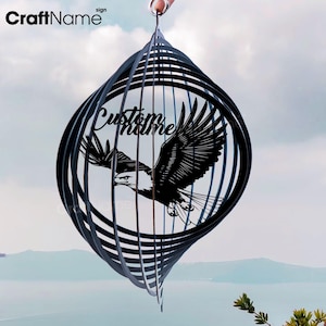 Könnte beinhalten: Schwarzer Windspinner aus Metall mit einer Silhouette eines Adlers im Flug. Der Spinner hat mehrere Ringe, die sich im Wind drehen. Der Text "Custom Name" ist auf dem Spinner sichtbar.