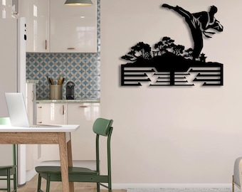 May include: A black metal wall art piece featuring a silhouette of a martial artist performing a high kick above a landscape of stylized trees and a small structure, with a series of horizontal cut-out lines forming a base below the scene.