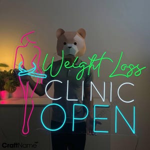 以下が含まれることがあります： ピンクの女性のシルエット、緑色の「Weight Loss Clinic」の文字、青色の「Open」の文字が入ったネオンサインです。