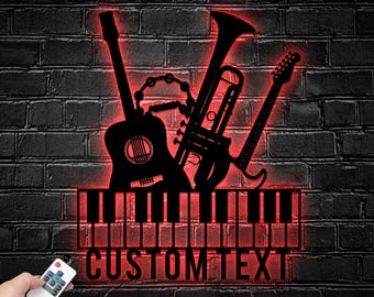 Puede incluir: Un letrero musical negro montado en la pared con siluetas de una guitarra acústica, una trompeta y una guitarra eléctrica sobre un teclado de piano. El letrero emite un brillo rojo e incluye el texto CUSTOM TEXT. Se ve un control remoto.
