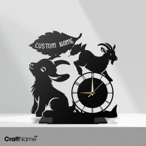 May include: A black laser-cut wall clock featuring two goat silhouettes and a large leaf shape with the text CUSTOM NAME. The clock face is circular with white numerals and gold hands, positioned below one of the goats on a flat base.