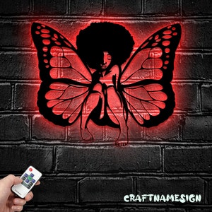 May include: Black silhouette of a woman with an afro hairstyle and butterfly wings, illuminated in red. The silhouette is against a brick wall background. The image includes the text "CRAFTNAMESIGN".